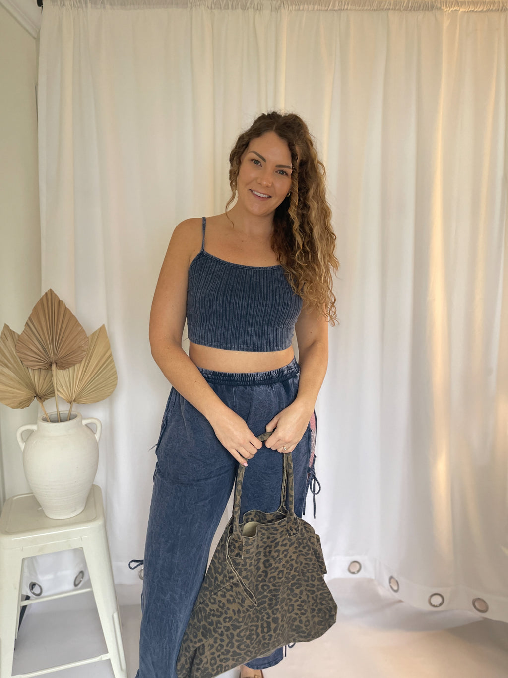 Woman holding a leopard print bag in a room with white curtains and a plant.