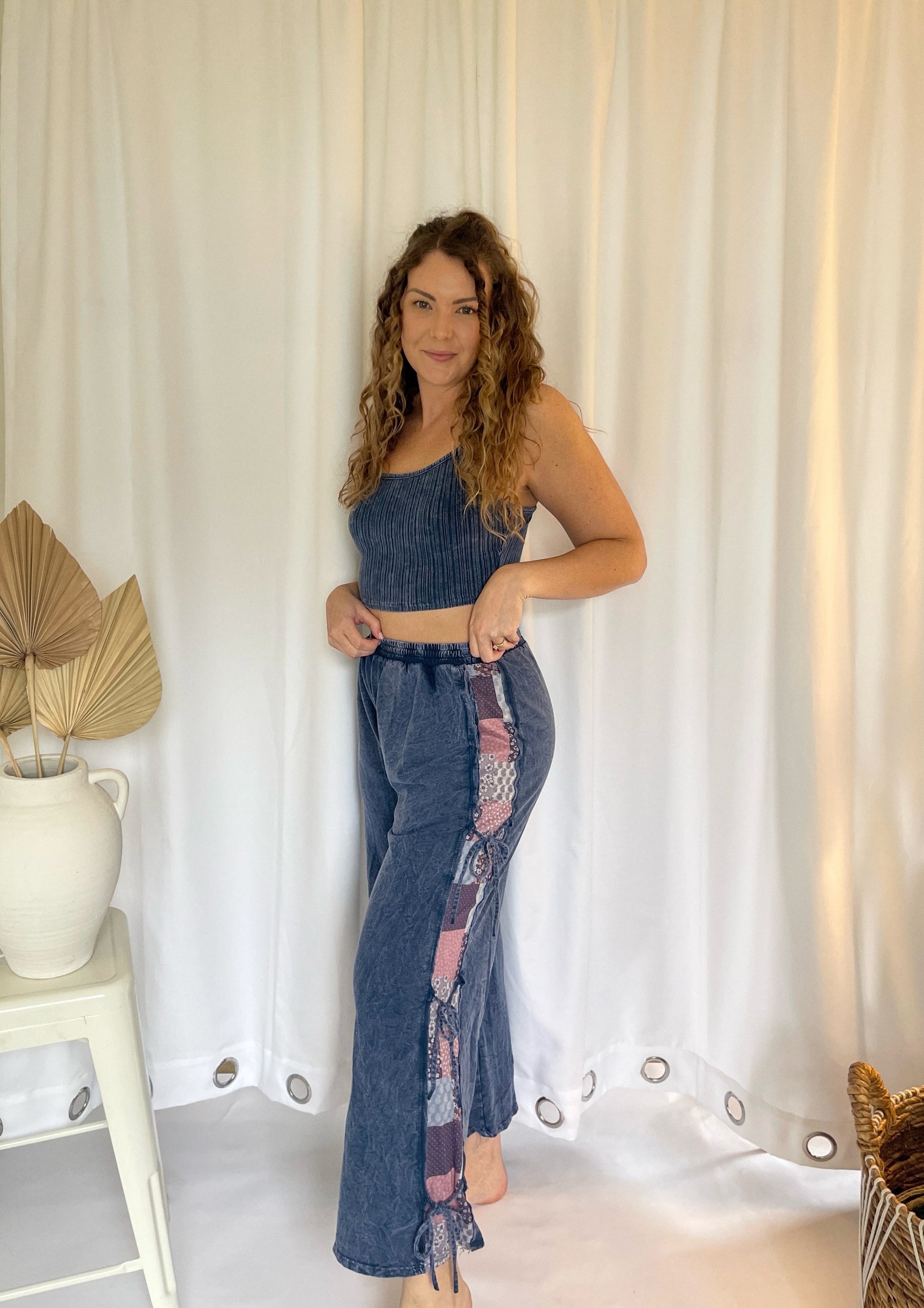 Woman wearing a denim outfit standing against a white curtain.